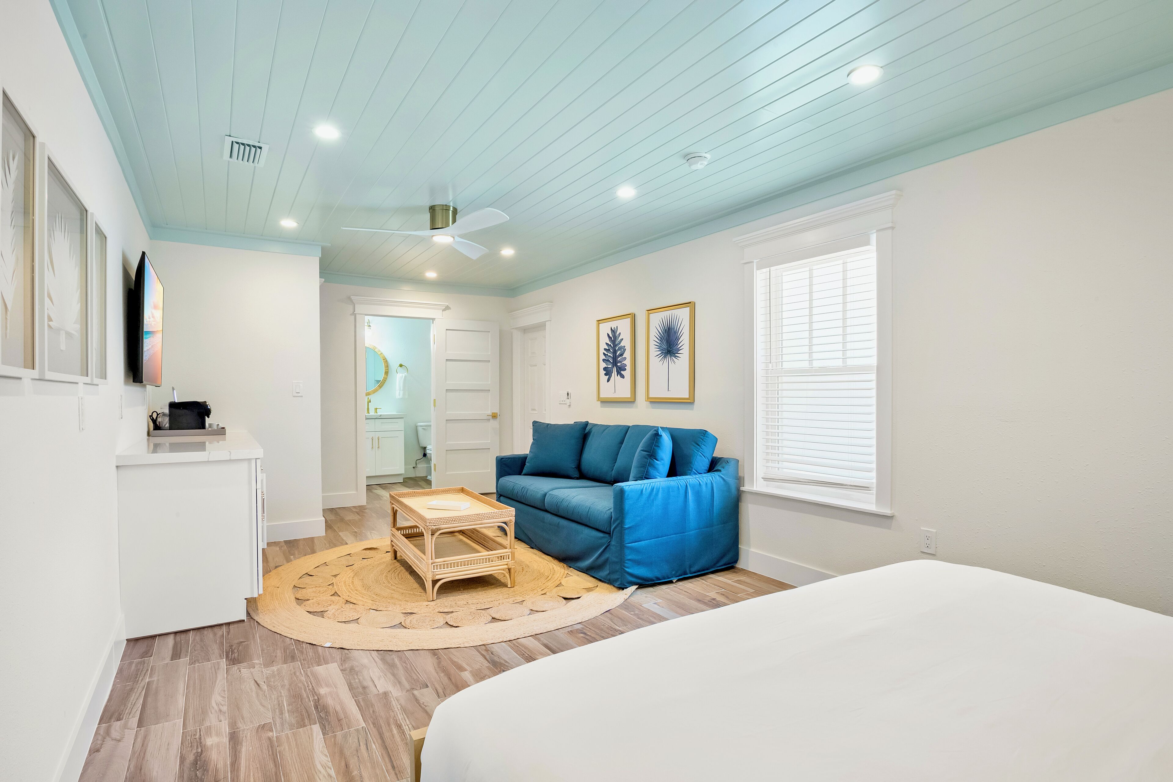 A bedroom with a bed, a blue sofa, a wooden coffee table, and a white dresser.
