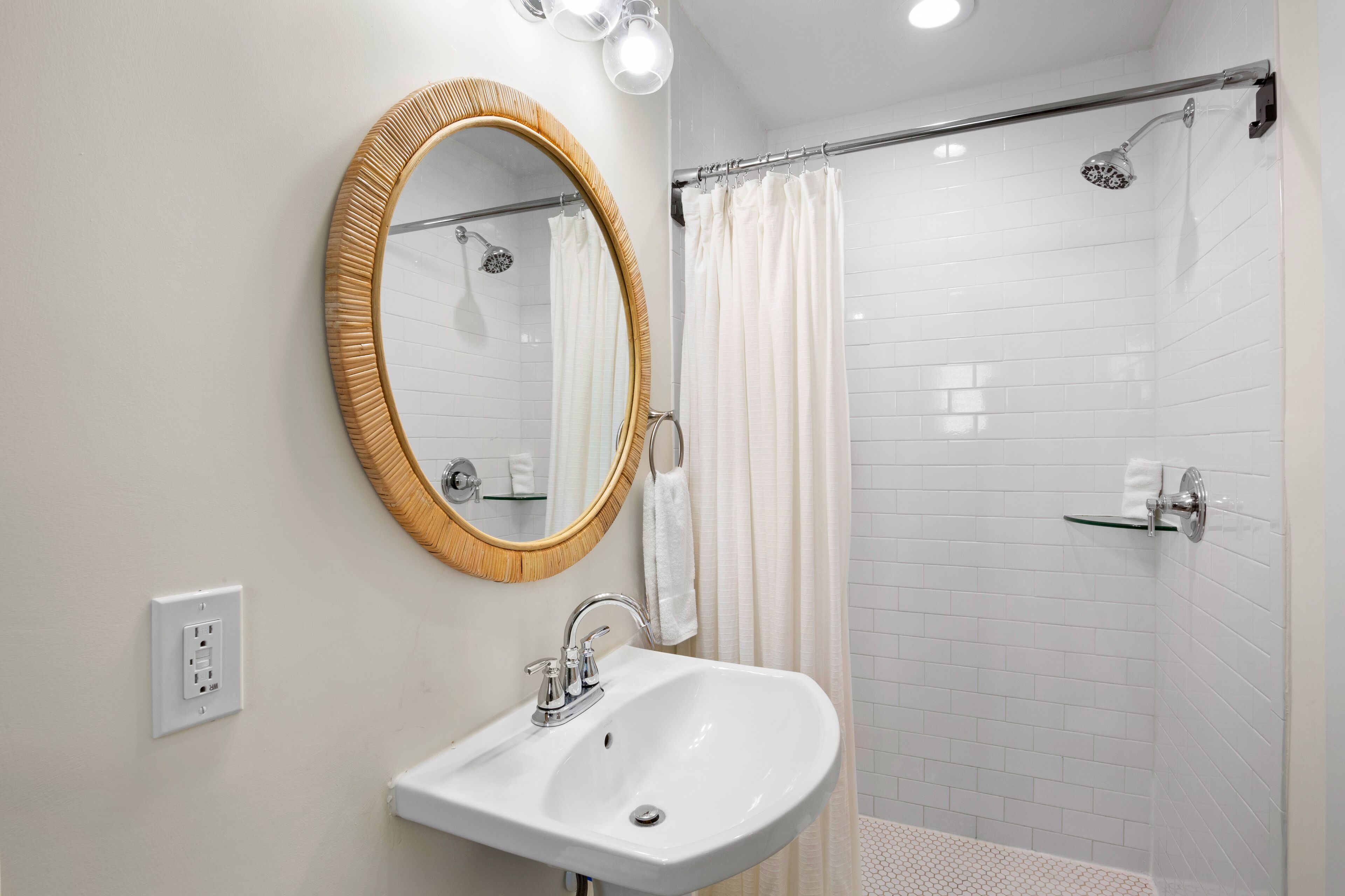 Une salle de bain avec un lavabo blanc, un miroir avec un cadre en bois, une douche avec une porte en verre et un porte-serviettes.