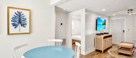 A dining area with a blue table and white chairs, a wooden cabinet, and a television displaying a scenic view.