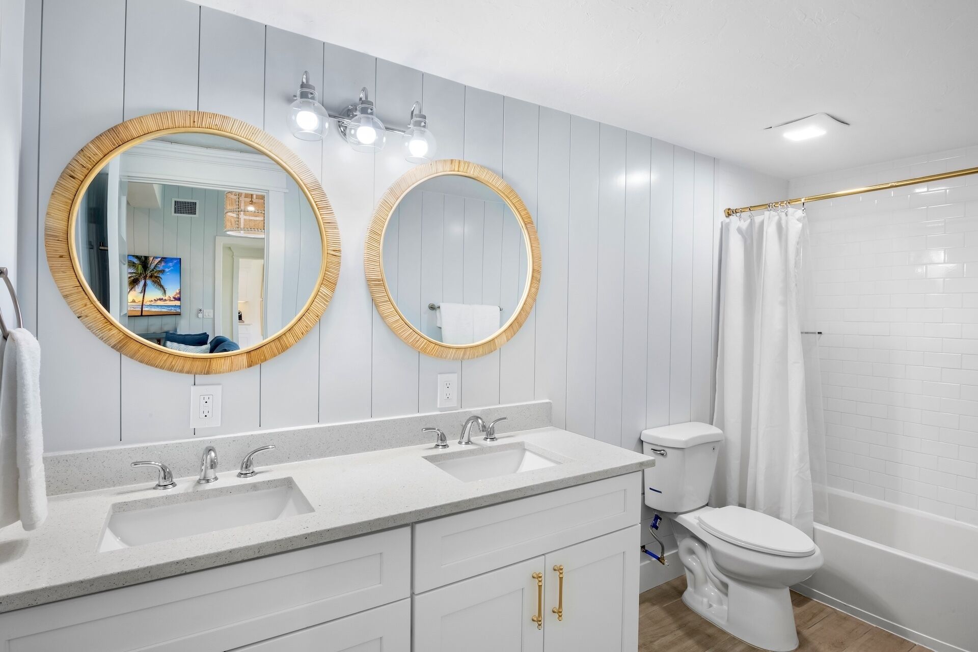 A bathroom with two round mirrors with gold frames, a white sink with two faucets, a toilet, and a shower with a white curtain.