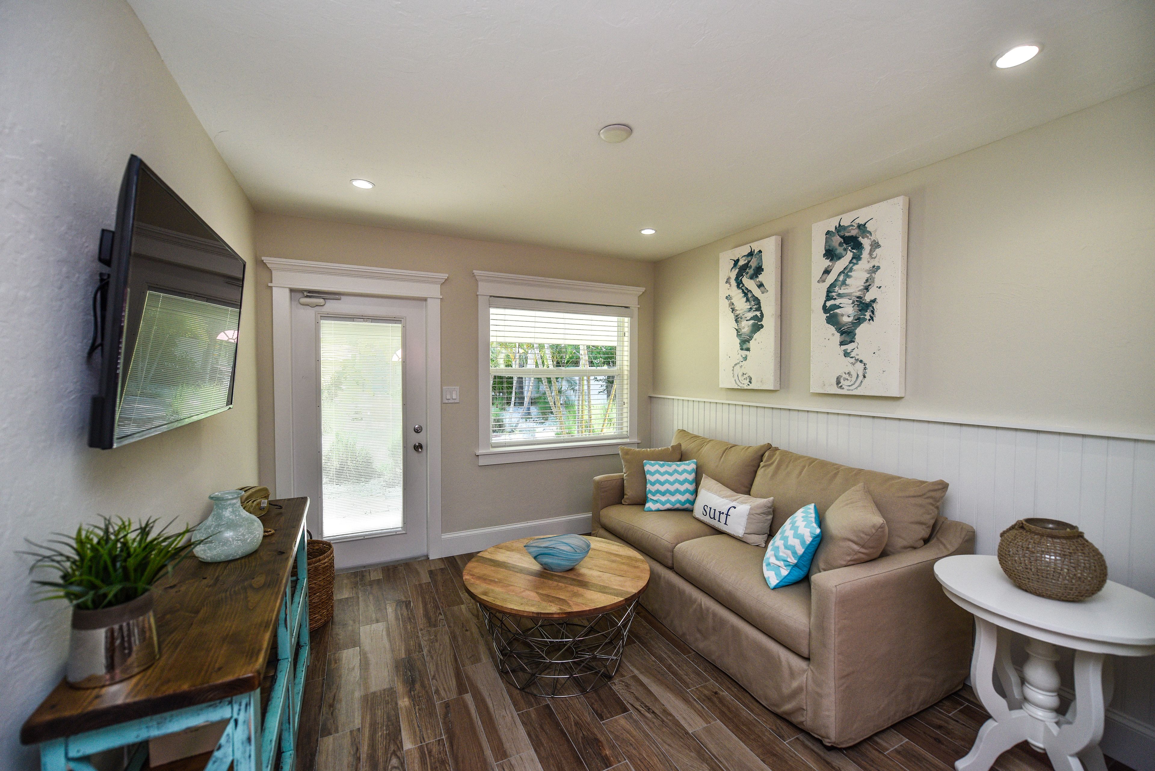 A living room with a beige sofa, a coffee table, and a TV mounted on the wall.