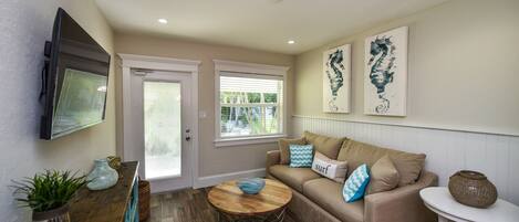 A living room with a beige sofa, a coffee table, and a TV mounted on the wall.