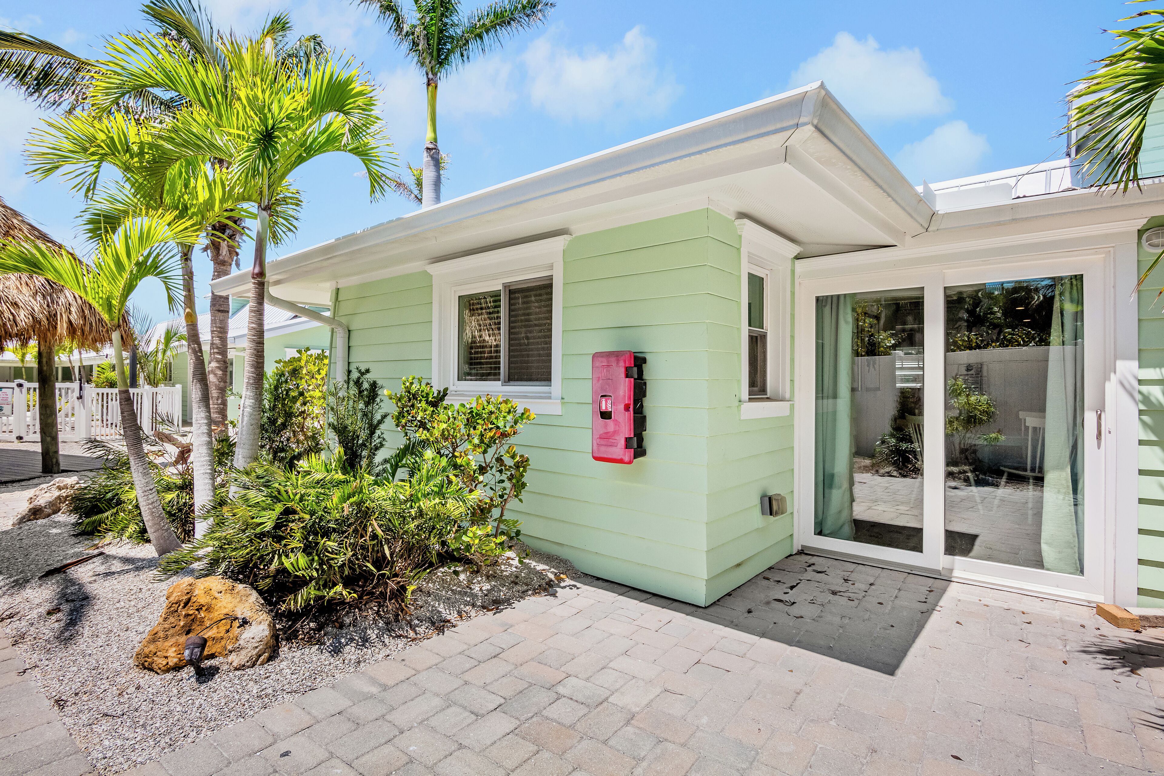 A light green house with a small porch, palm trees, and a red mailbox.