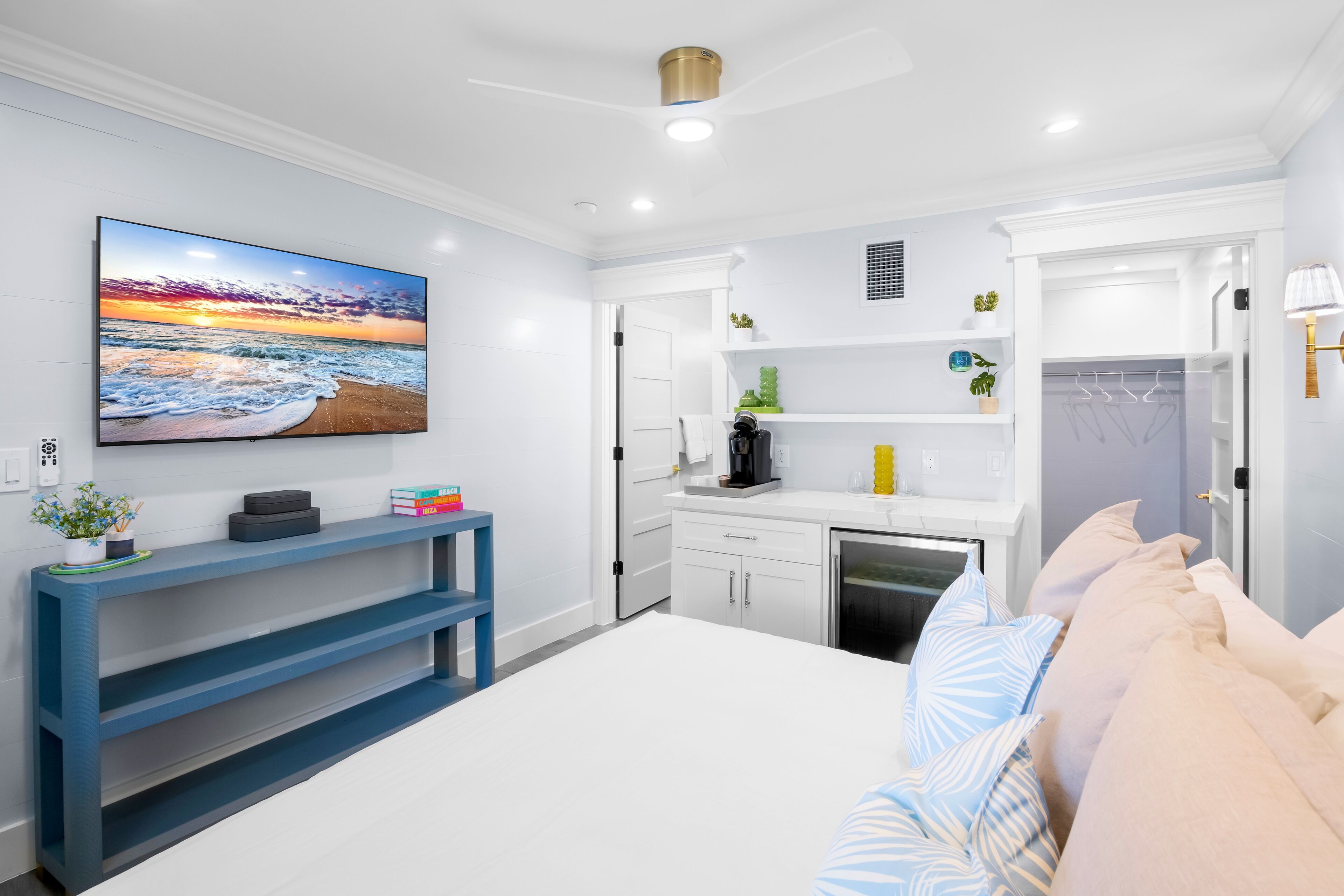 Een moderne hotelkamer met een groot bed, een flatscreen televisie, een blauwe console tafel, een kitchenette en een inloopkast.