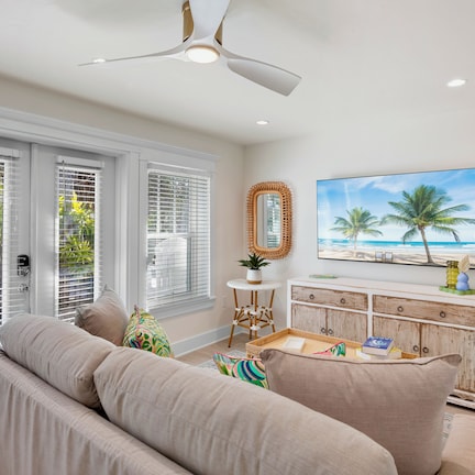 A living room with a beige sofa, a wooden console table, a ceiling fan, and a beach-themed painting.