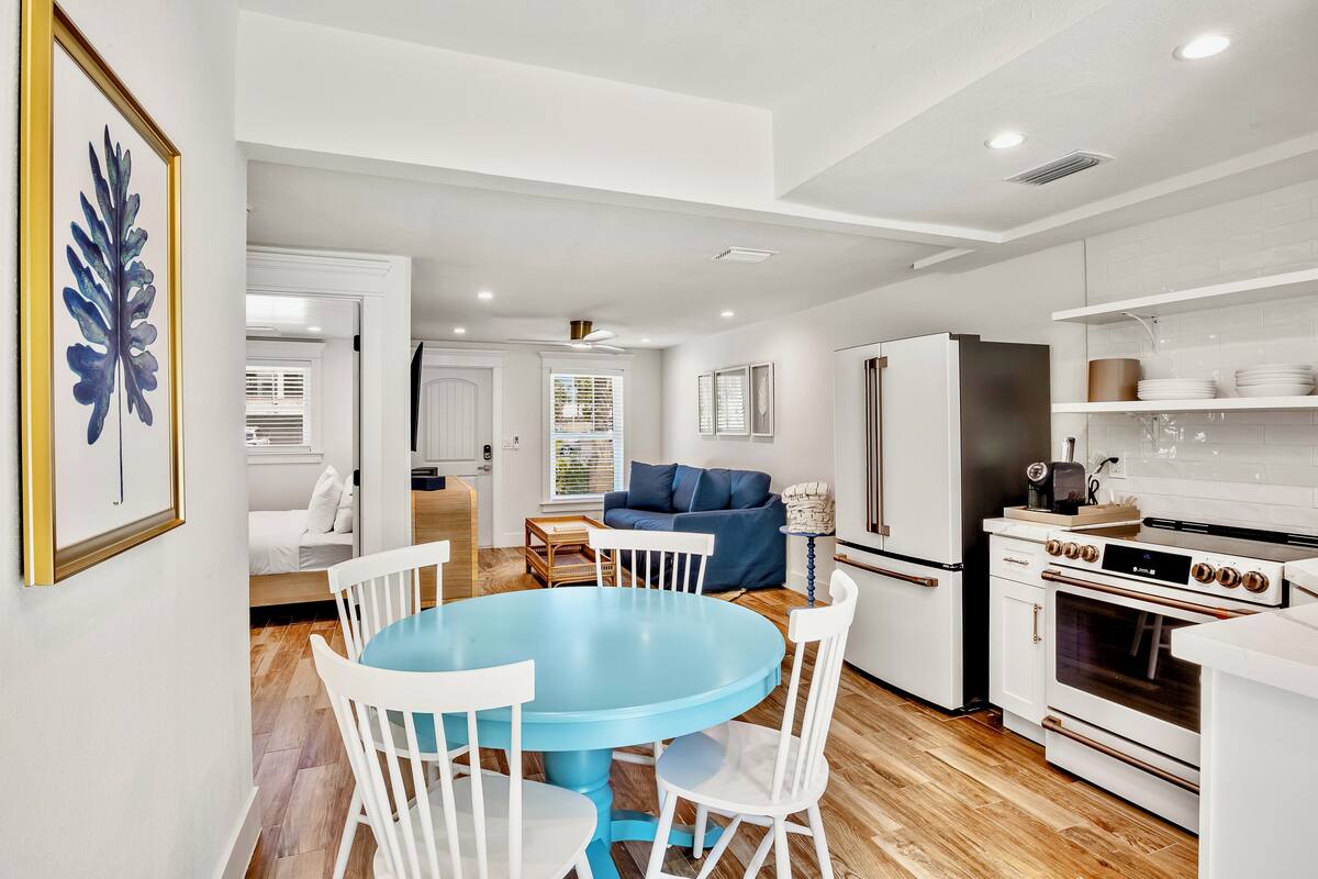 A modern kitchen with white cabinetry, a blue dining table, and a blue sofa in the living area.