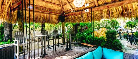 An outdoor patio with wooden furniture, a hanging light fixture, and lush greenery.