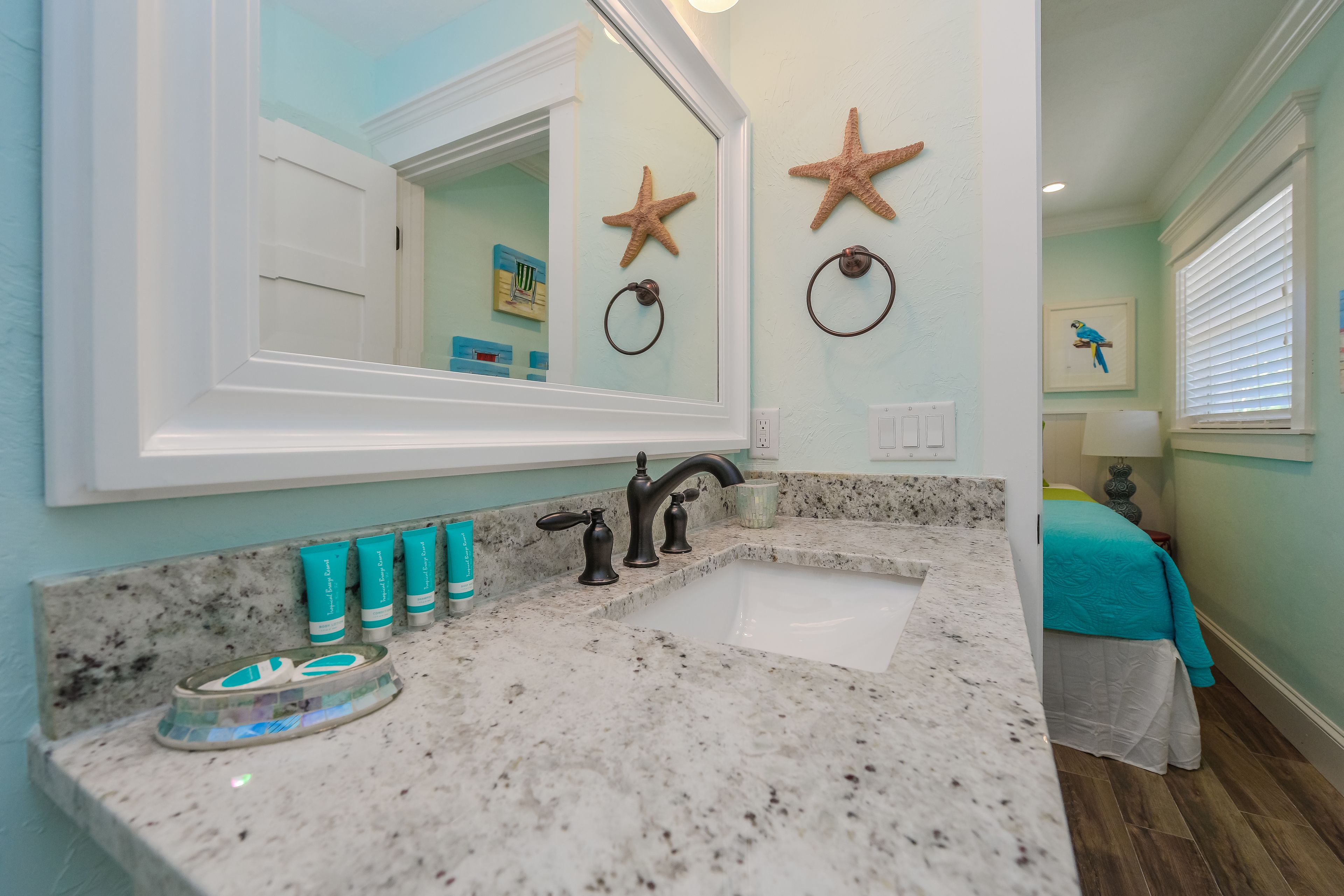 A bathroom with a granite countertop, a white sink, and a large mirror. There are starfish decorations on the wall and a towel ring.