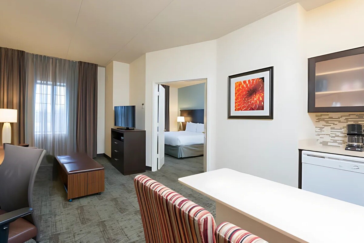 Habitación de hotel con escritorio, silla, cama y kitchenette.