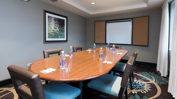 A conference room with a long table, chairs, water bottles, and a projector screen. - Staybridge Suites Chicago-Oakbrook Terrace by IHG (Villa Park)
