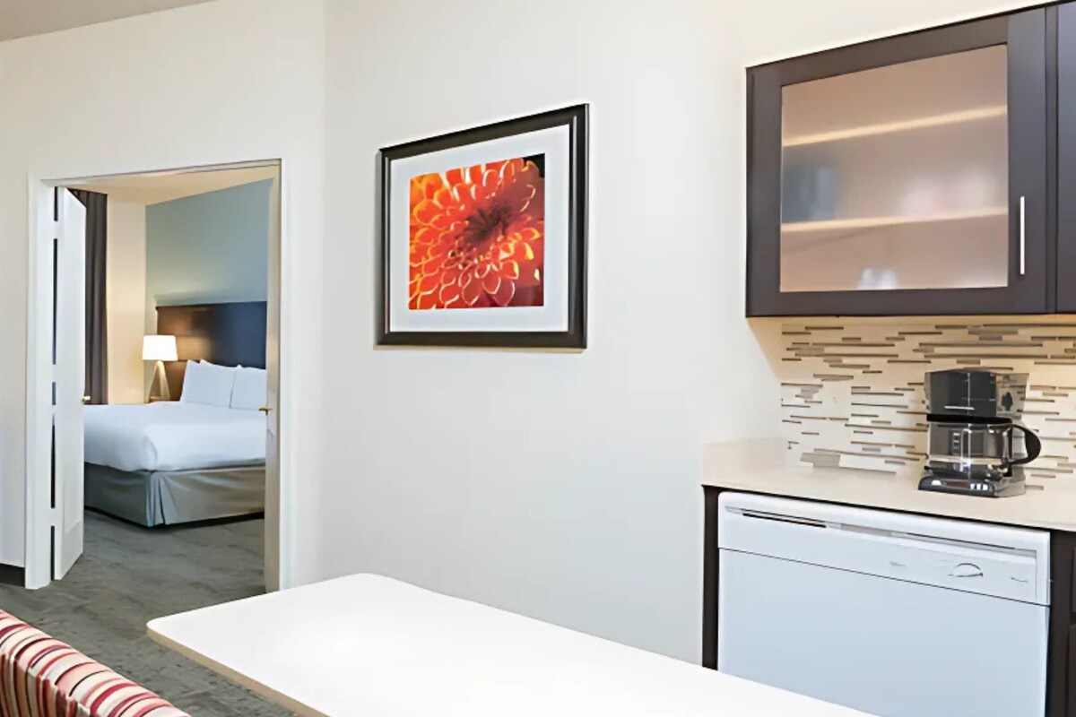 Una habitación de hotel con cama, escritorio, cafetera y un cuadro en la pared.