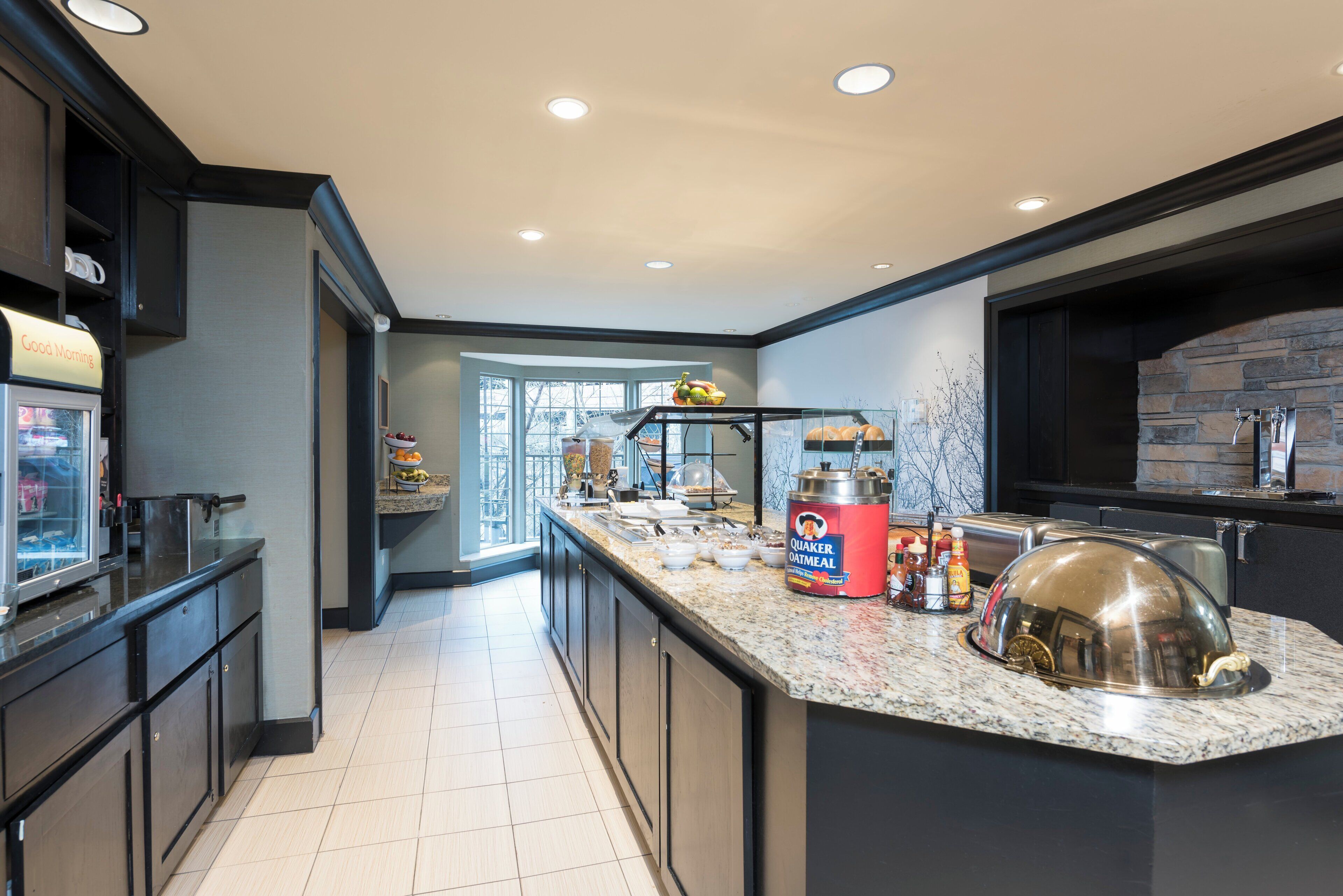 A modern kitchen with a granite countertop, a Quaker Oatmeal dispenser, and a stone backsplash.