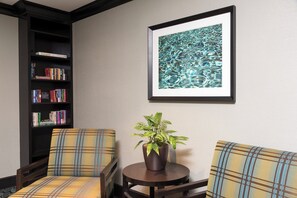 Un espacio de lectura con dos sillones, una mesita, una planta en maceta y una estantería llena de libros.