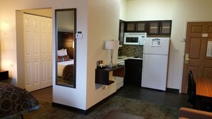 A compact hotel room with a bed, a small kitchenette, a mirror, and a door. - Staybridge Suites Chicago-Oakbrook Terrace by IHG (Villa Park)