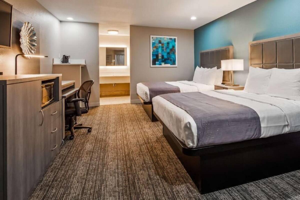 A hotel room with a large bed, a desk, a chair, a dresser, and a painting on the wall.
