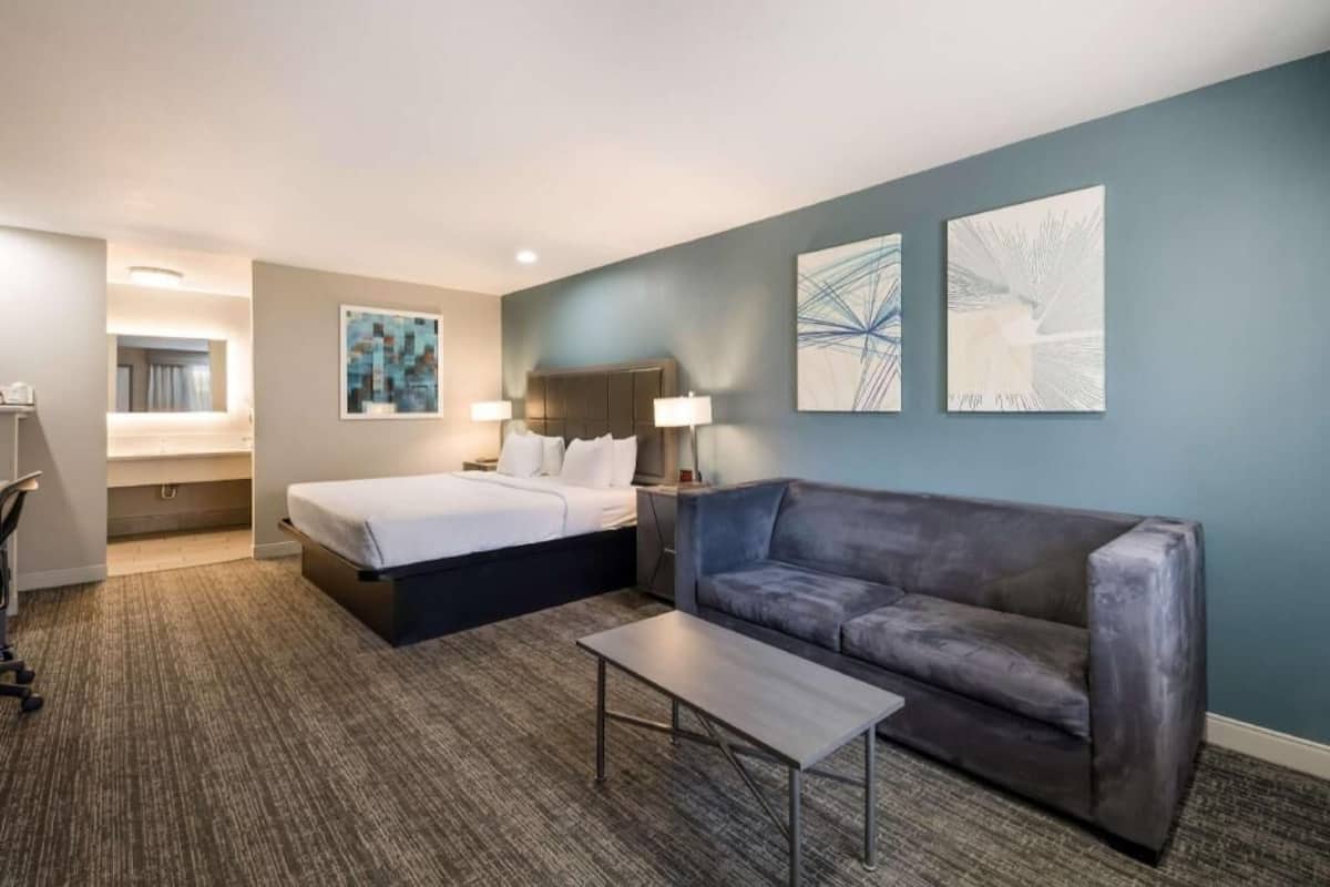 A hotel room with a bed, a sofa, a coffee table, and artwork on the walls.