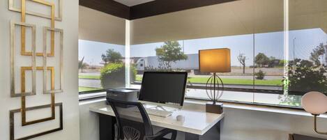 A modern office space with a desk, computer, chair, and a window with a view of a building and greenery.