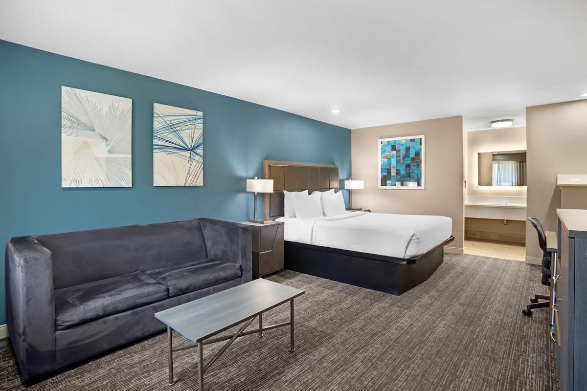 A hotel room with a bed, a sofa, a small table, and artwork on the walls.