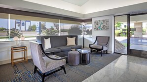 Eine moderne Lobby mit einem grauen Sofa, gemusterten Sesseln, einem kleinen Tisch und einem großen Fenster mit Blick ins Freie.