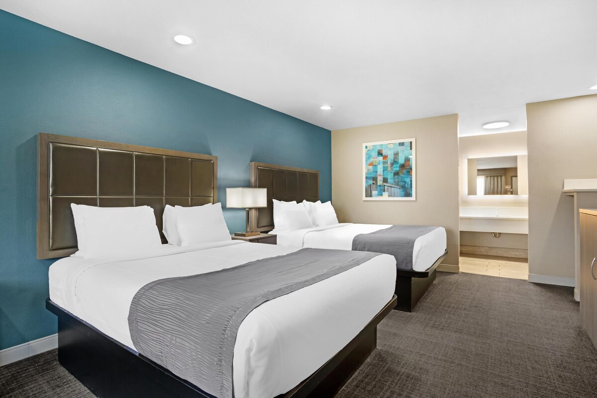 Quarto de hotel com duas camas, um quadro grande na parede e banheiro visível por uma porta aberta.