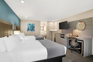Habitación de hotel con dos camas, un escritorio con silla, un televisor montado en la pared y una pieza decorativa grande sobre el escritorio.