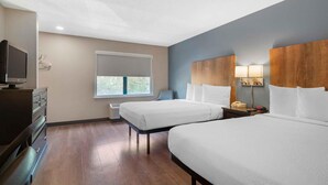 A hotel room with two beds, a TV, a desk, and a window with a view.