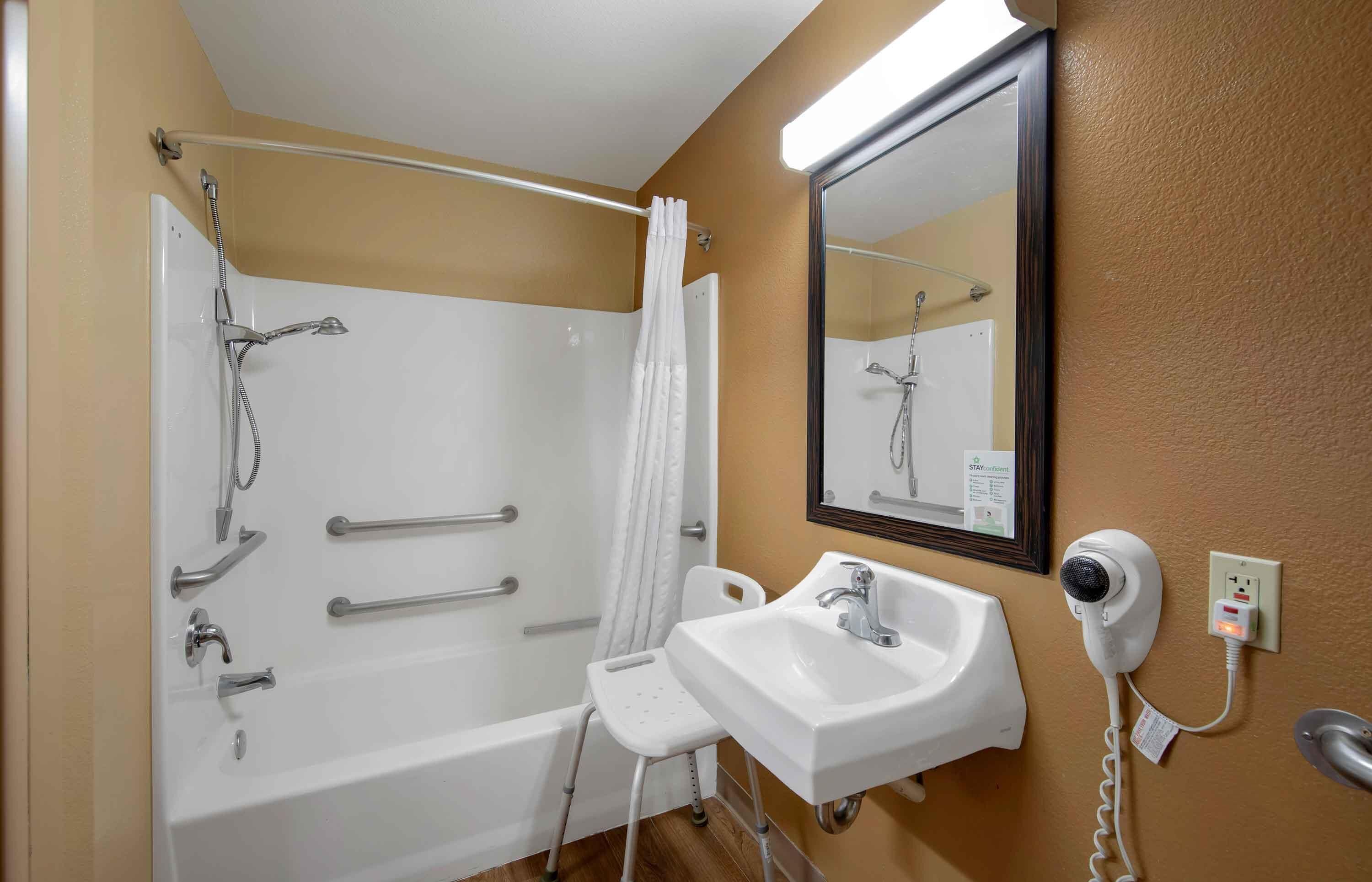 A bathroom with a bathtub, a shower, a sink, a mirror, and a hairdryer.