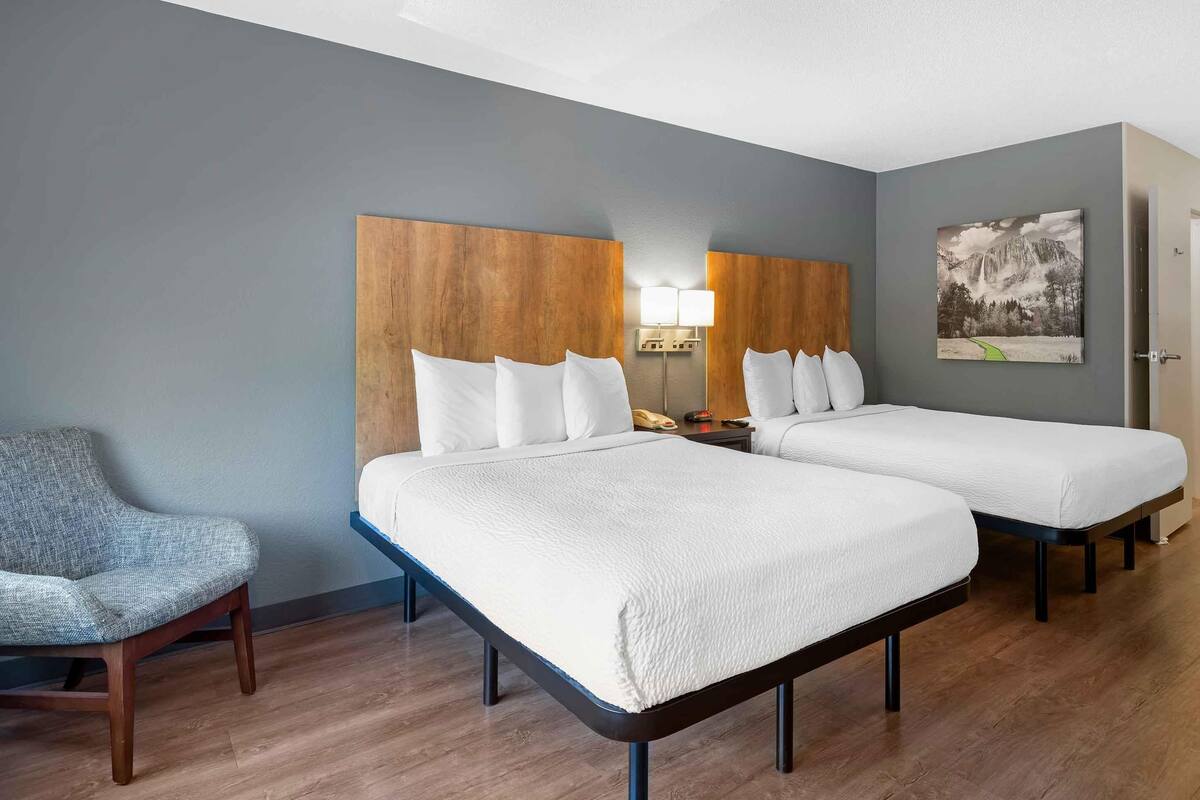 Une chambre d’hôtel avec deux lits, une chaise, une lampe et un tableau au mur.