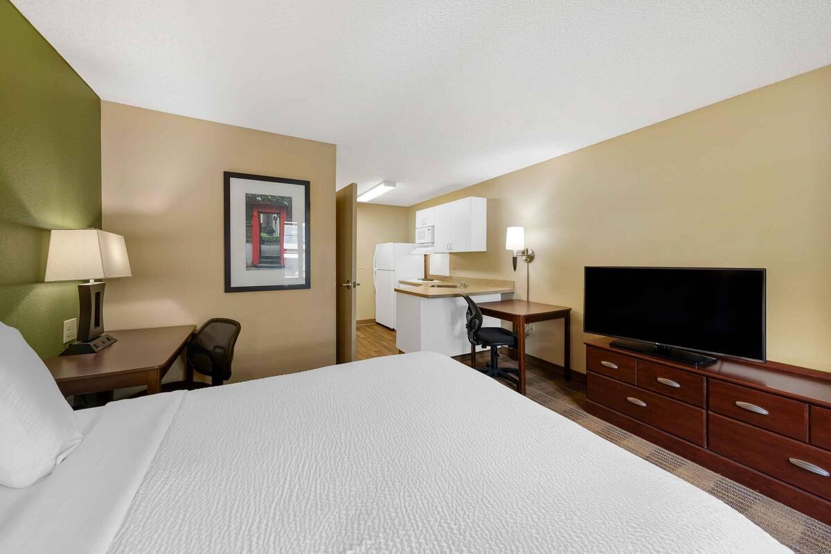 Une chambre d’hôtel équipée d’un lit, d’un bureau, d’une chaise, d’une télévision et d’une kitchenette.