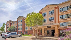 A multi-story hotel with a central lobby, parking lot, and a tree in front.