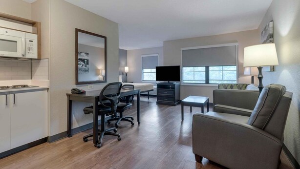 A hotel room with a kitchenette, a dining area, a sofa, a TV, and a lamp.