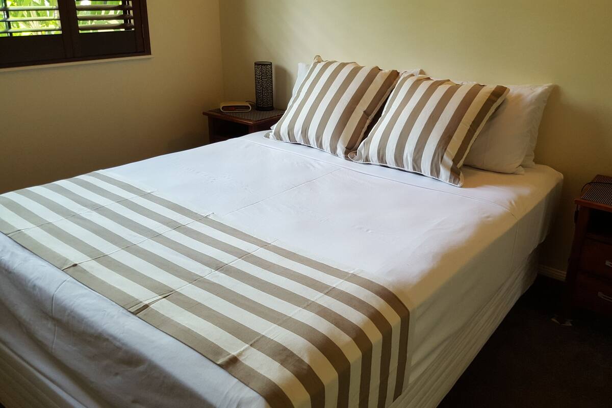 A neatly made bed with striped bedding, two bedside tables with lamps, and a window with blinds.