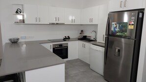 A modern kitchen with white cabinets, stainless steel appliances, and a grey countertop. - Nautilus Holiday Apartments (Port Douglas)