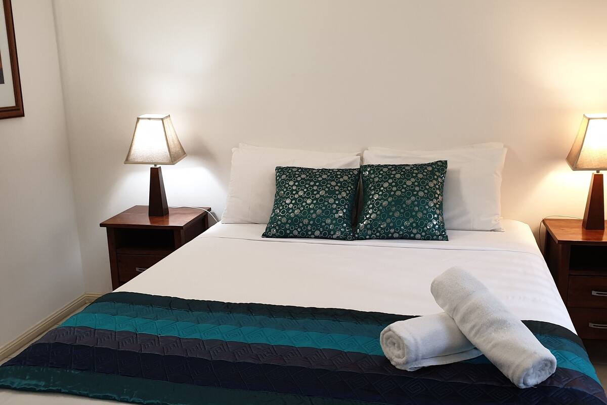 A neatly made bed with a striped blanket, two pillows, and a rolled towel. There are two bedside tables with lamps.