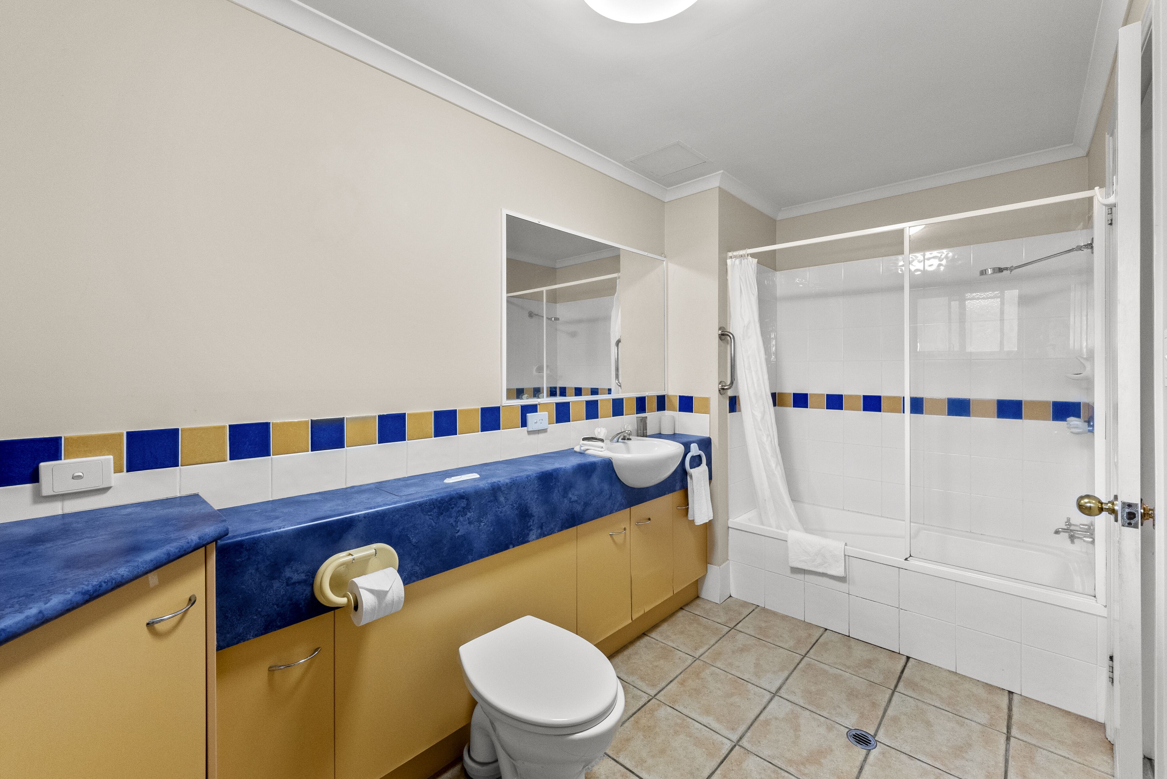 Une salle de bain avec un plan de toilette bleu, un lavabo blanc, des toilettes et une douche à parois de verre.