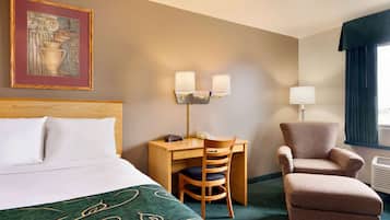A hotel room with a bed, a desk with a chair, a lamp, and a window with curtains.