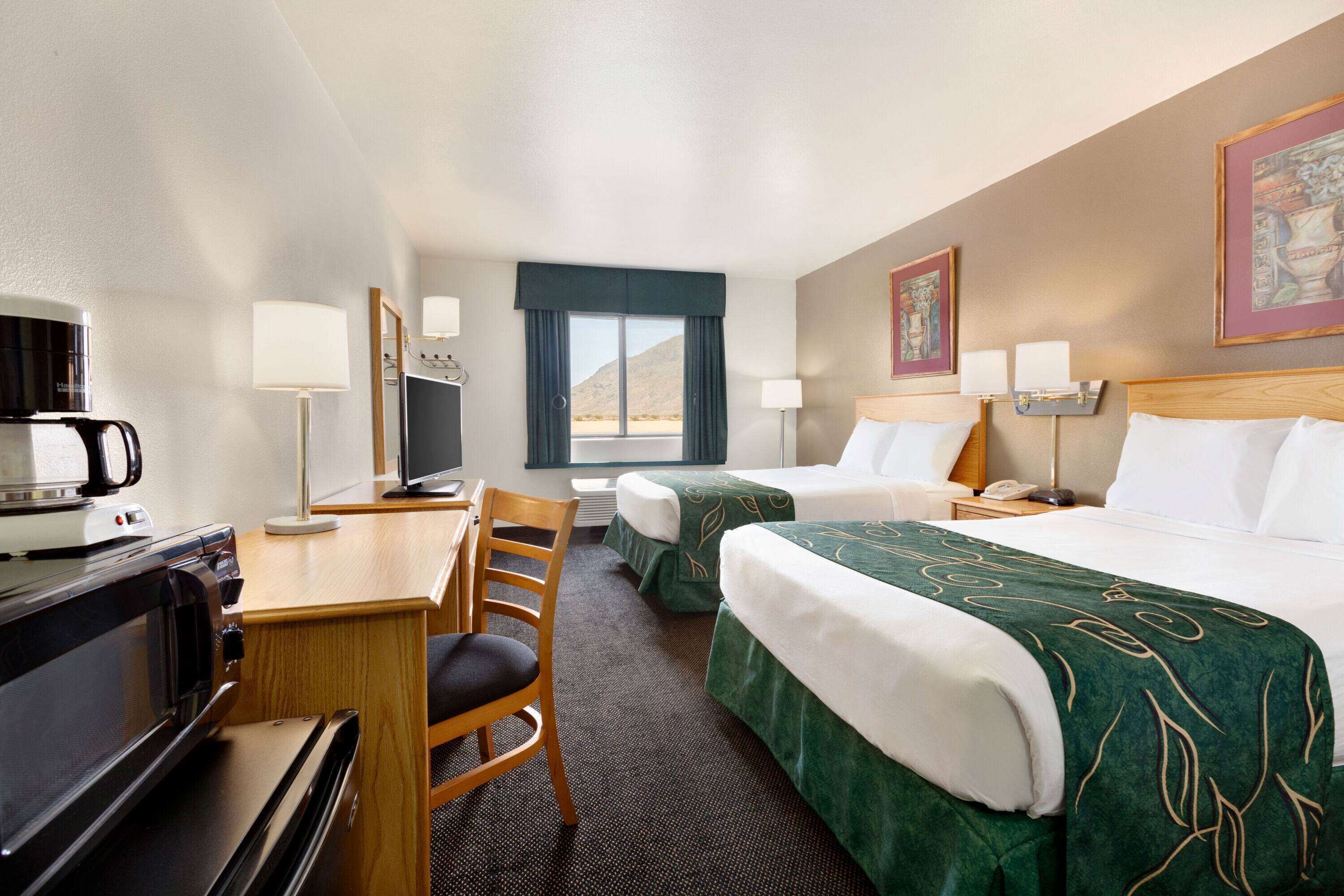 A hotel room with two beds, a desk with a coffee maker, a chair, and a television.