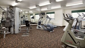 Een fitnessruimte met diverse trainingsapparaten, vloerbedekking en spiegelwanden.