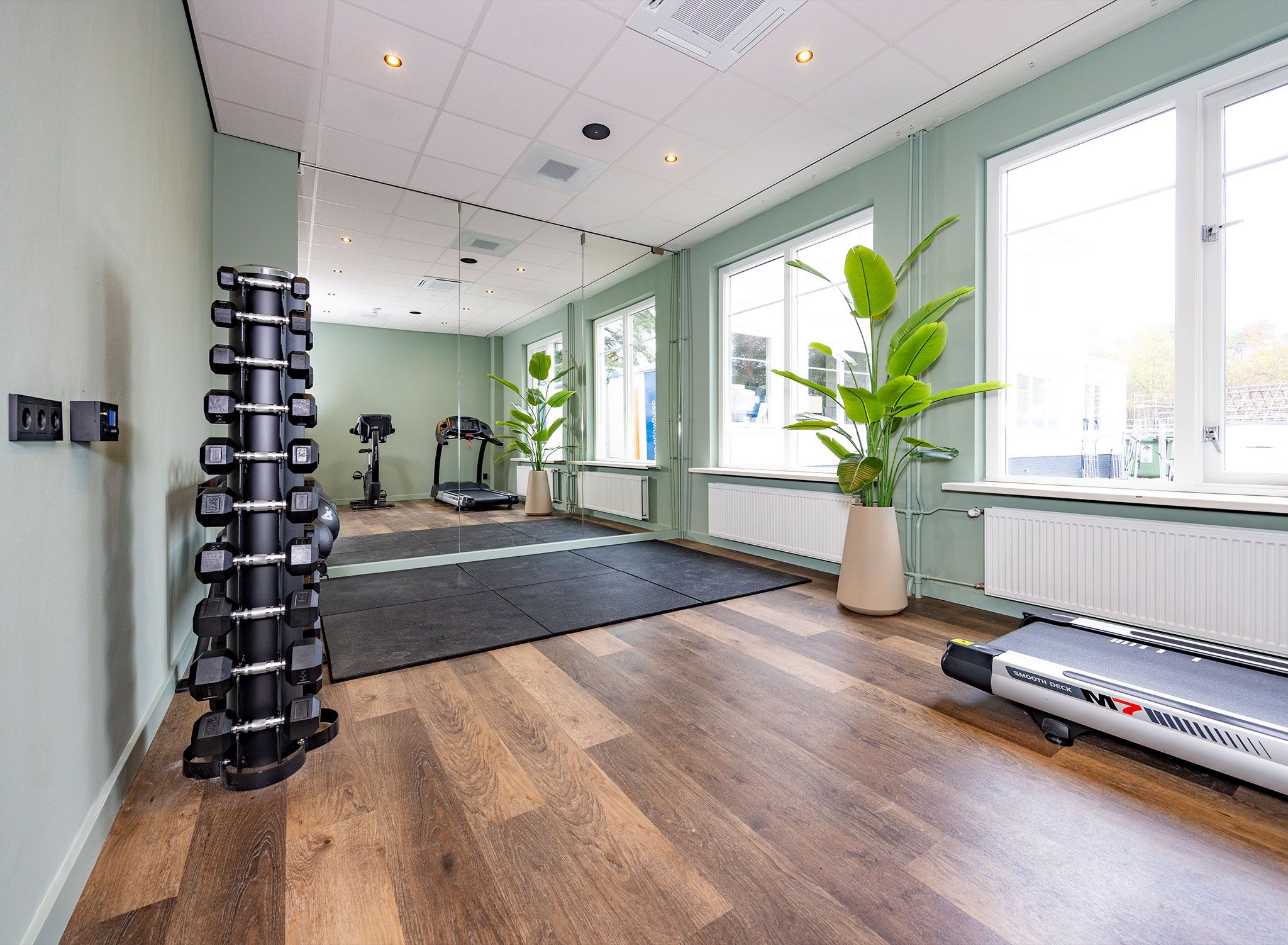 Een sportschool met fitnessapparatuur, een loopband en een groot raam.