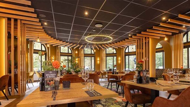 Un restaurante con mesas y sillas de madera, ventanas amplias y un candelabro.