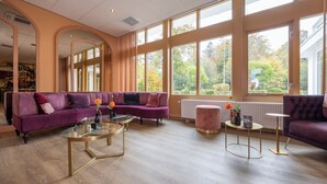 Un salón espacioso con un ventanal grande, un sofá morado, una mesa de centro de cristal y una mesita redonda.