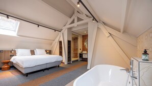 Un dormitorio moderno con una cama grande, un vestidor y un baño con bañera independiente.