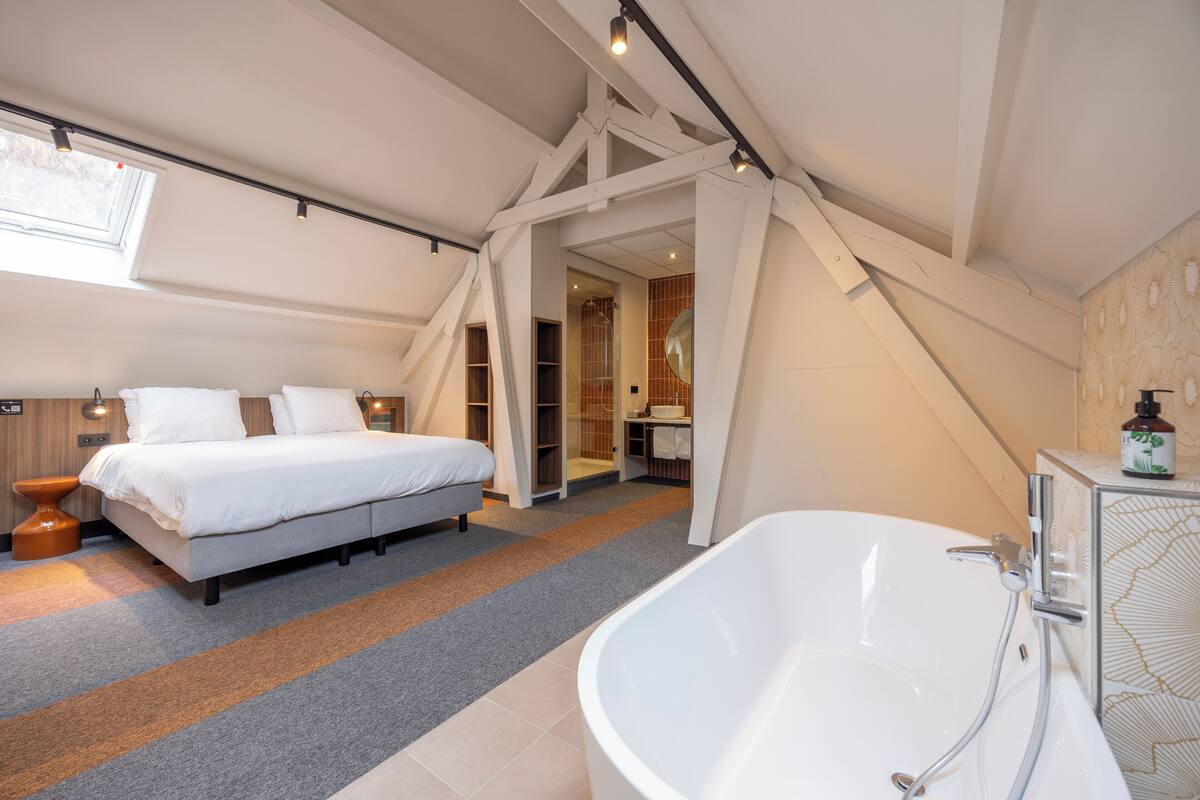 A modern bedroom with a large bed, a walk-in closet, and a bathroom with a freestanding bathtub.