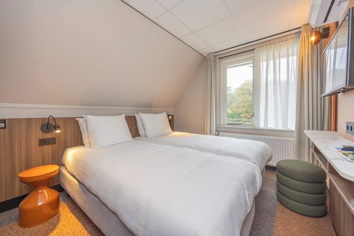 Une chambre d’hôtel avec un grand lit, un bureau, une chaise et une fenêtre avec des rideaux.