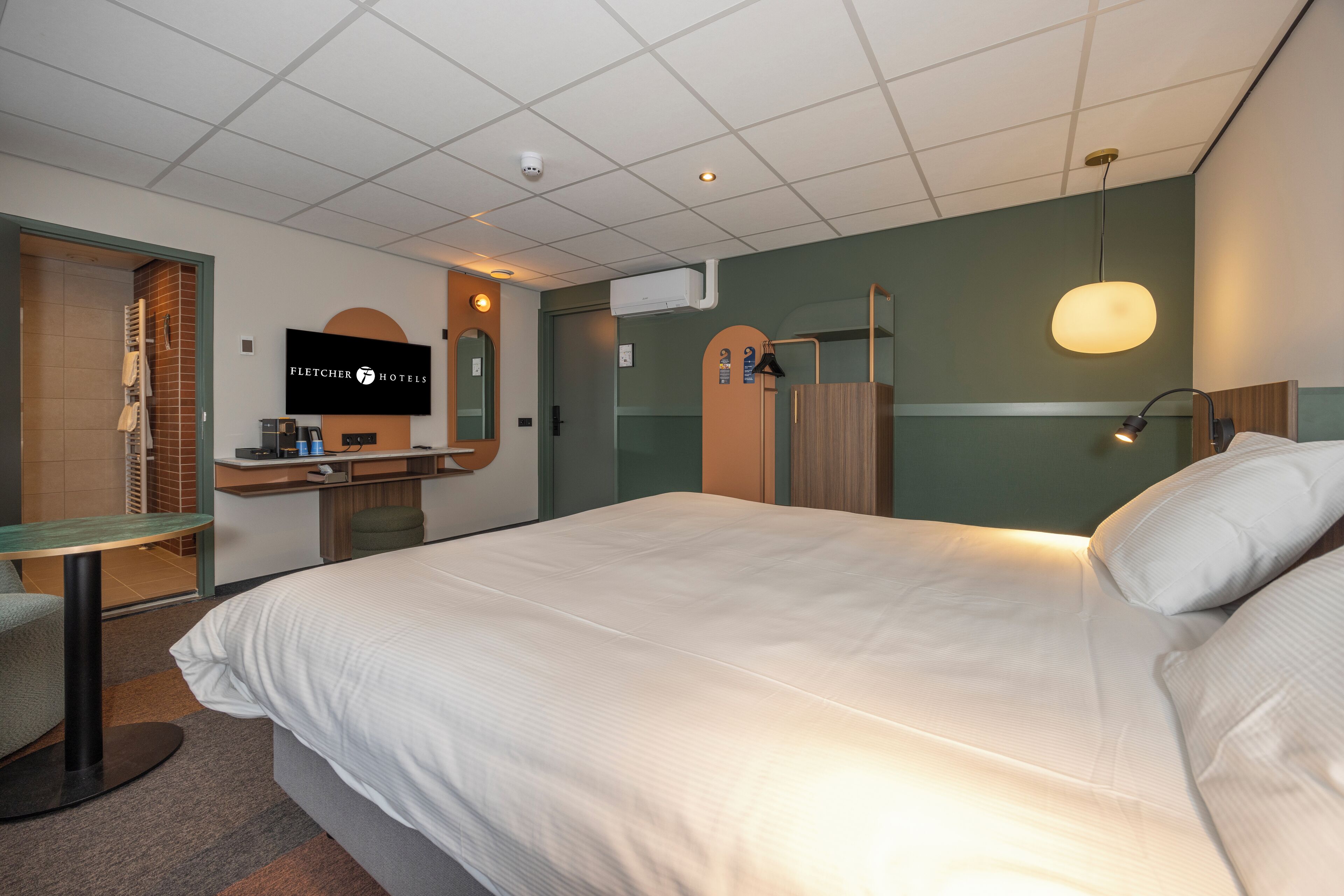 Habitación de hotel con una cama grande, un escritorio con silla, un televisor y un espejo.