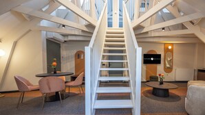 Interior de hotel con una escalera central, una mesa redonda con sillas y un área de descanso con un sofá.
