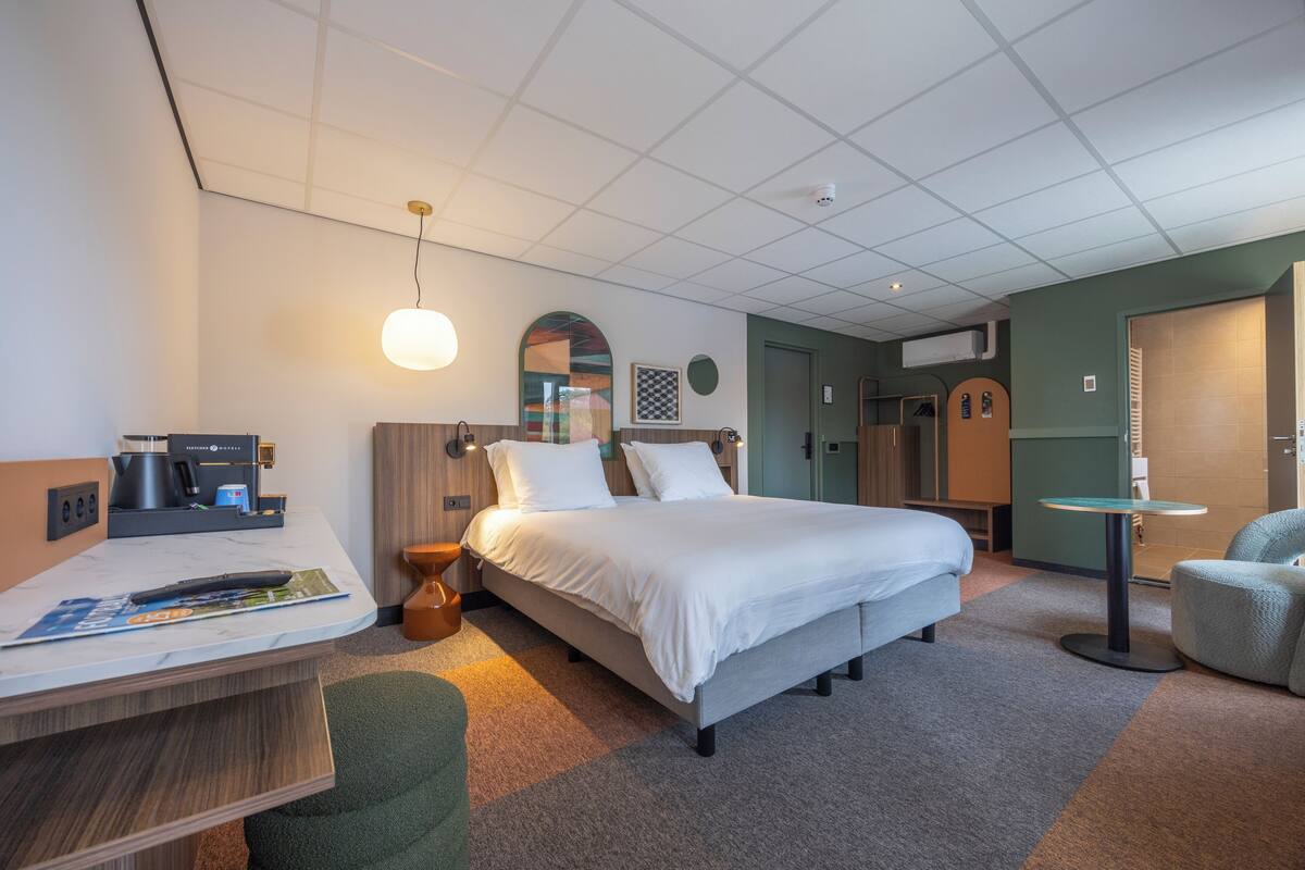 A hotel room with a bed, bedside table, lamp, and a small round table.