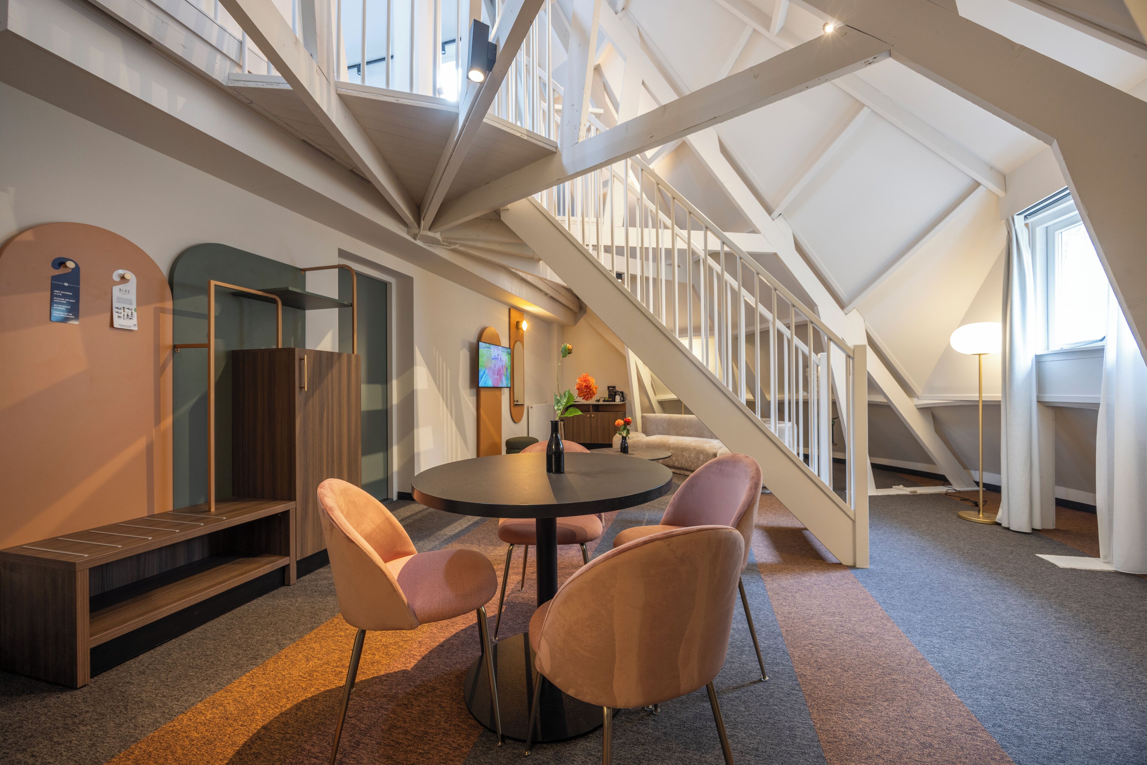 A modern interior with a round table, four chairs, a bench, and a staircase.