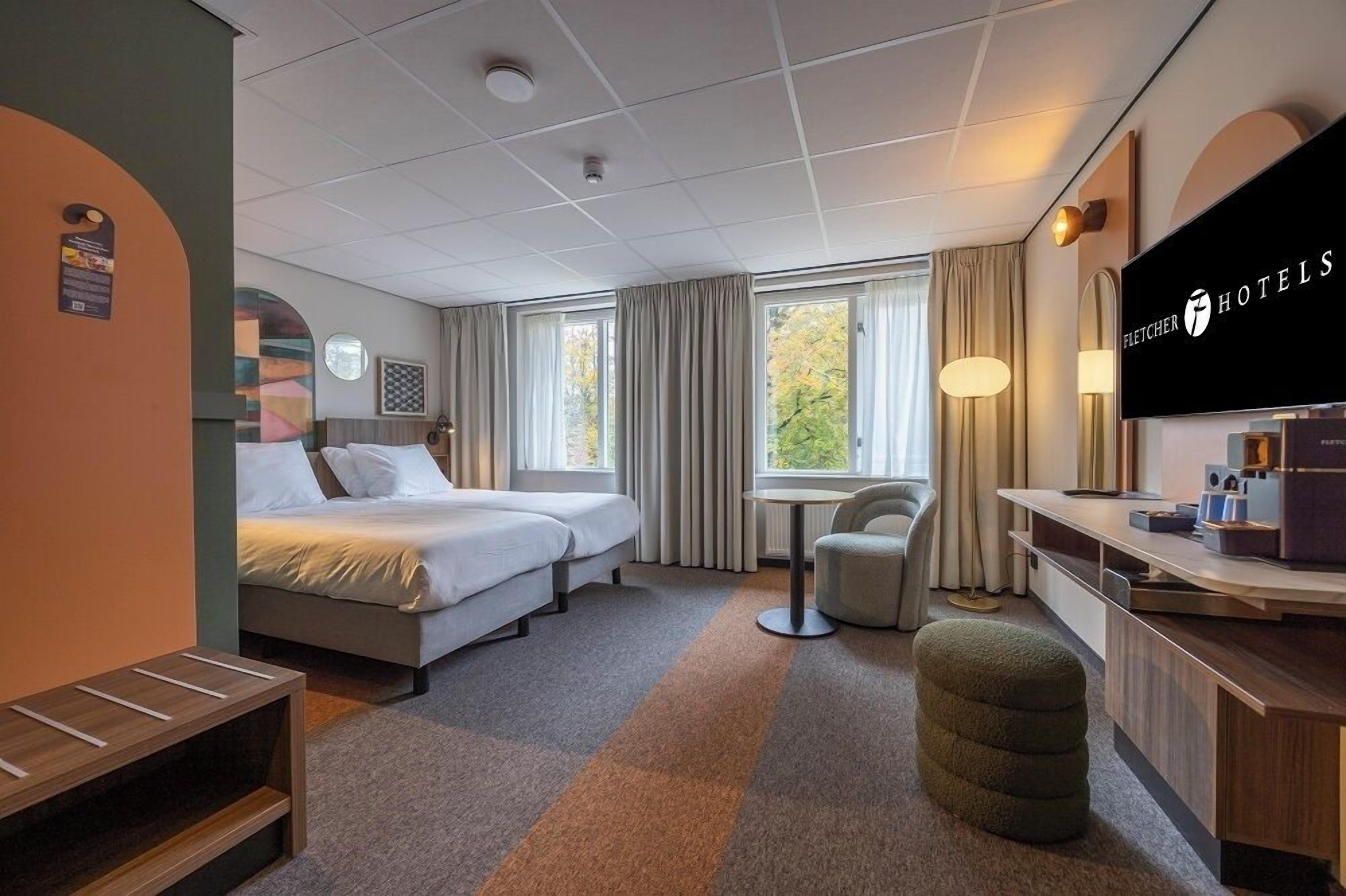A hotel room with two beds, a desk, a chair, a TV, and a window with curtains.
