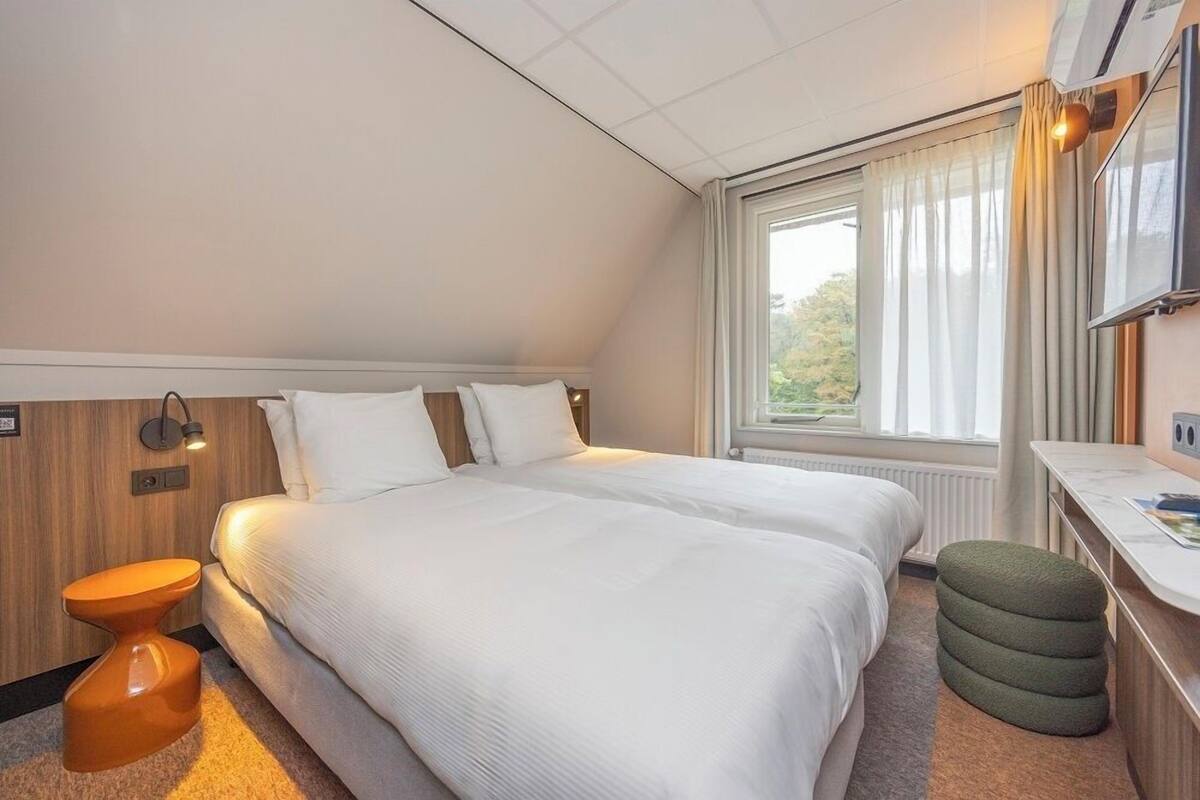 A hotel room with a large bed, a desk, a chair, and a window with curtains.